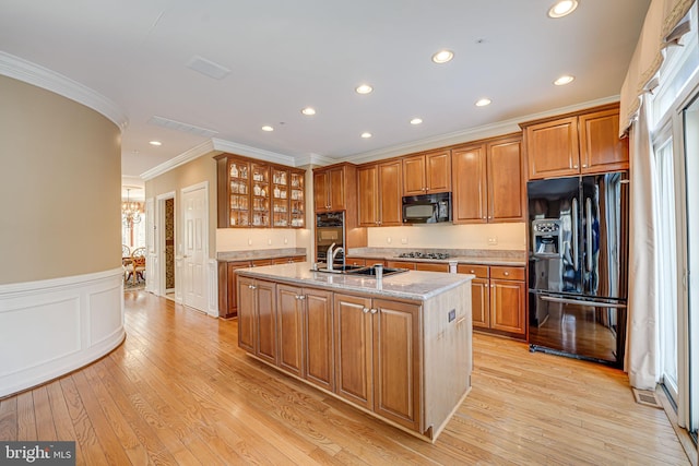 kitchen with crown molding, sink, light stone counters, a center island with sink, and black appliances