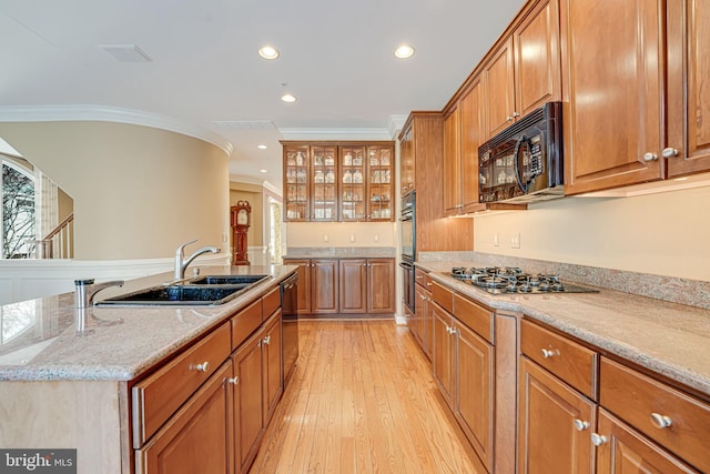 kitchen with crown molding, sink, light stone counters, an island with sink, and black appliances