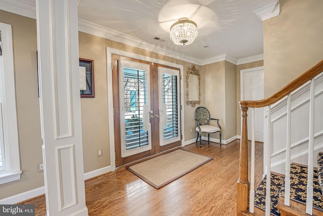 foyer entrance with an inviting chandelier, crown molding, french doors, and light wood-type flooring