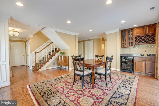 dining space with light hardwood / wood-style floors, indoor wet bar, crown molding, and wine cooler