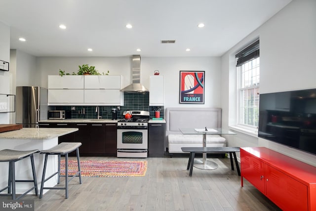 kitchen featuring light wood-type flooring, stainless steel appliances, sink, wall chimney range hood, and white cabinets