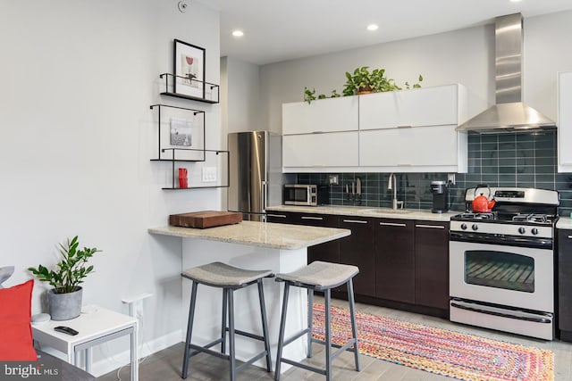 kitchen featuring wall chimney exhaust hood, light hardwood / wood-style floors, white cabinetry, a breakfast bar area, and gas stove