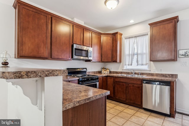 kitchen featuring appliances with stainless steel finishes, a sink, a peninsula, dark countertops, and recessed lighting