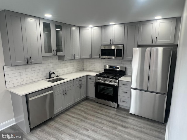 kitchen with light hardwood / wood-style floors, stainless steel appliances, decorative backsplash, sink, and gray cabinets