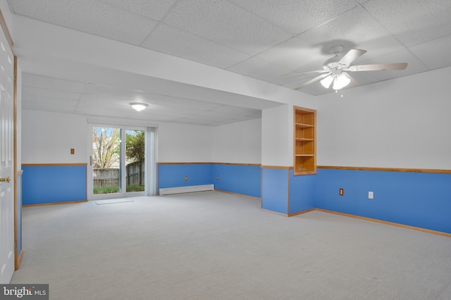 empty room with a drop ceiling, ceiling fan, carpet floors, and a baseboard radiator