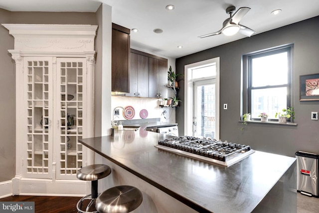 kitchen featuring dark brown cabinetry, ceiling fan, stainless steel gas stovetop, a breakfast bar area, and hardwood / wood-style flooring