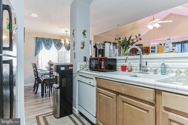 kitchen with ceiling fan with notable chandelier, light hardwood / wood-style floors, tile countertops, black appliances, and sink