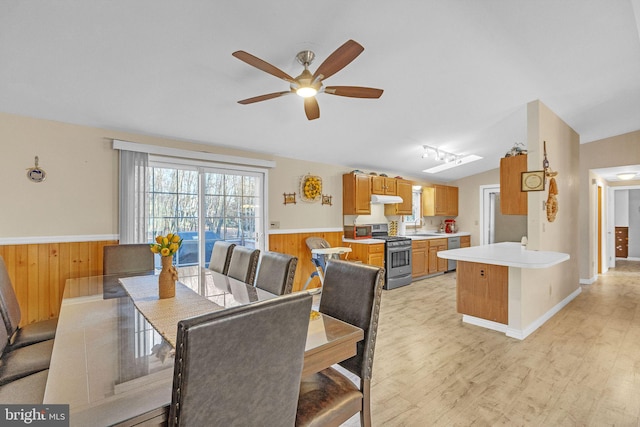 dining area featuring lofted ceiling, sink, wooden walls, ceiling fan, and light wood-type flooring