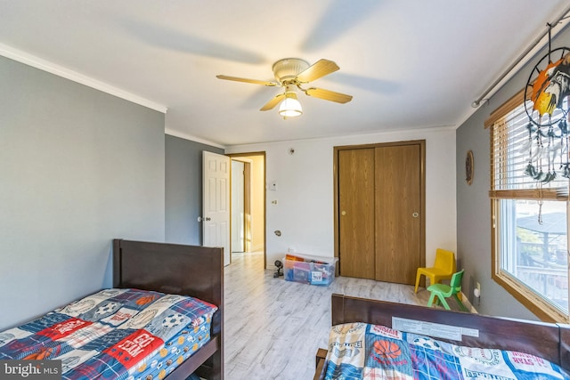 bedroom with ceiling fan, light hardwood / wood-style floors, ornamental molding, and a closet