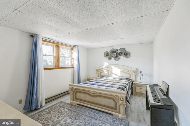 bedroom with a drop ceiling, light hardwood / wood-style floors, and a baseboard radiator