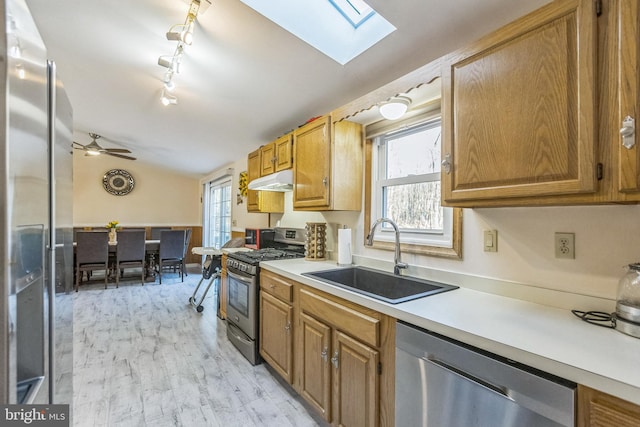 kitchen with lofted ceiling with skylight, sink, light hardwood / wood-style flooring, ceiling fan, and appliances with stainless steel finishes