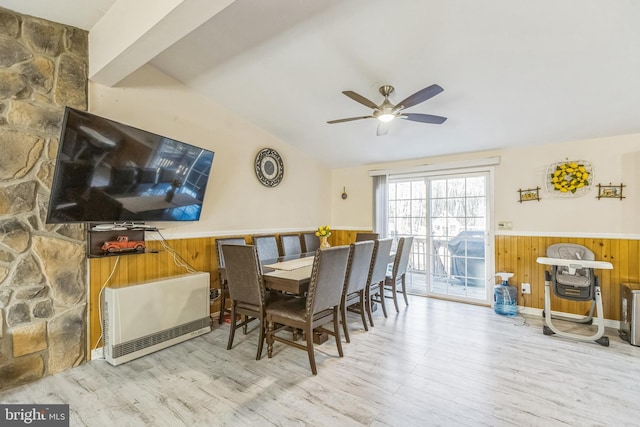 dining space featuring ceiling fan, wooden walls, vaulted ceiling, and light wood-type flooring