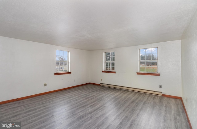 empty room featuring wood-type flooring, a baseboard radiator, plenty of natural light, and a textured ceiling