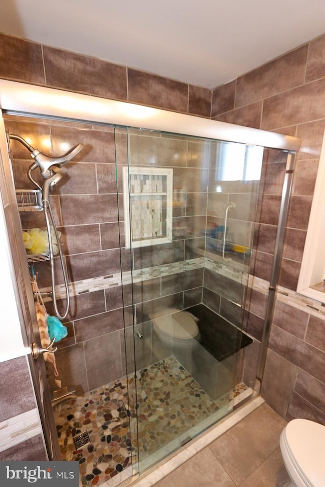 bathroom featuring toilet, tile patterned flooring, and a shower with shower door