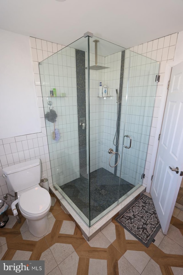 bathroom featuring tile walls, toilet, tile patterned floors, and a shower with door