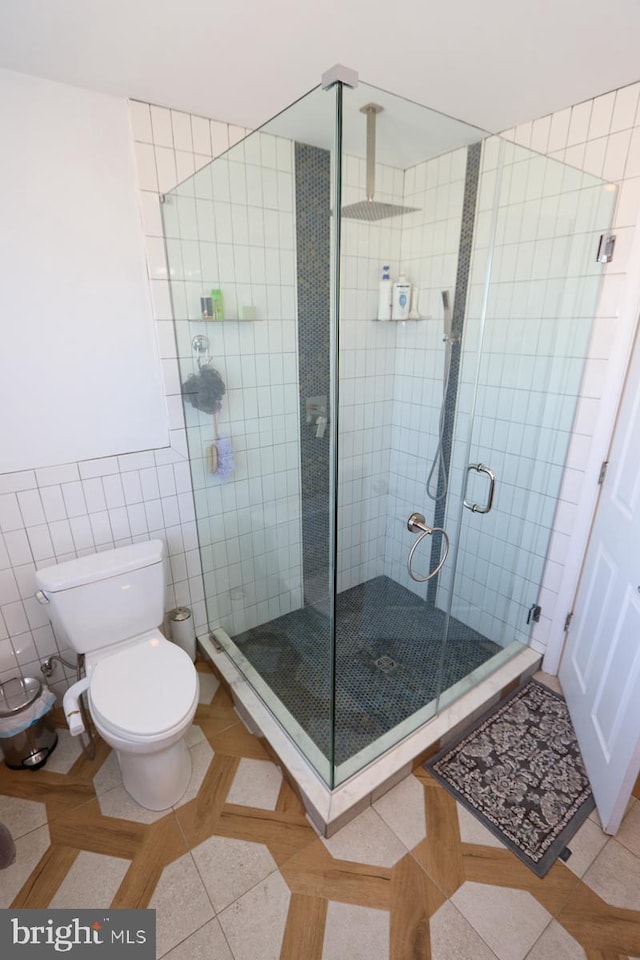 bathroom with tile walls, toilet, tile patterned floors, and a shower with shower door