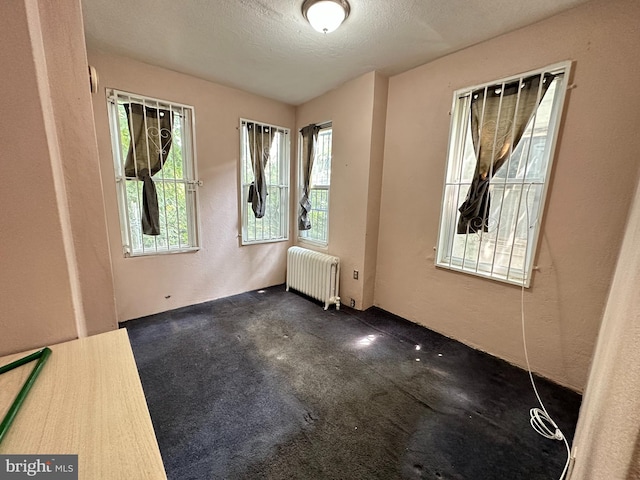 empty room featuring dark colored carpet, radiator heating unit, and a textured ceiling