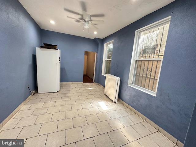 tiled spare room with radiator and ceiling fan