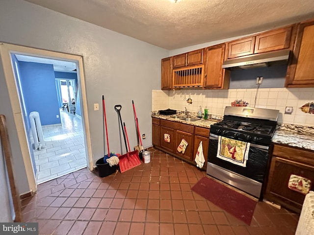 kitchen featuring dark tile patterned flooring, decorative backsplash, gas range, a textured ceiling, and sink