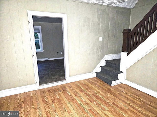 stairway featuring hardwood / wood-style flooring, wooden walls, and a baseboard radiator