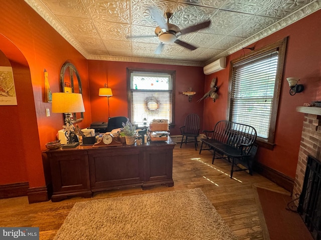 office area featuring a wall mounted air conditioner, hardwood / wood-style floors, a fireplace, and ceiling fan