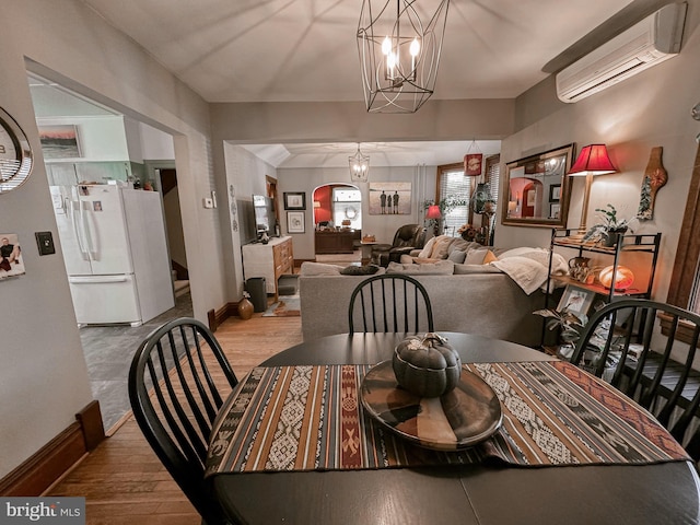 dining area featuring light hardwood / wood-style floors, a wall unit AC, and an inviting chandelier