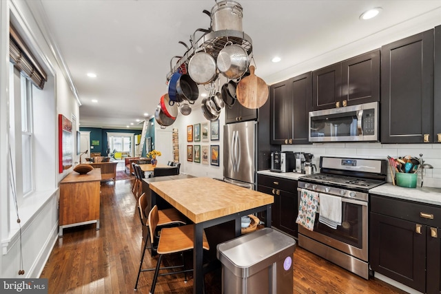 kitchen with ornamental molding, appliances with stainless steel finishes, dark hardwood / wood-style floors, and backsplash