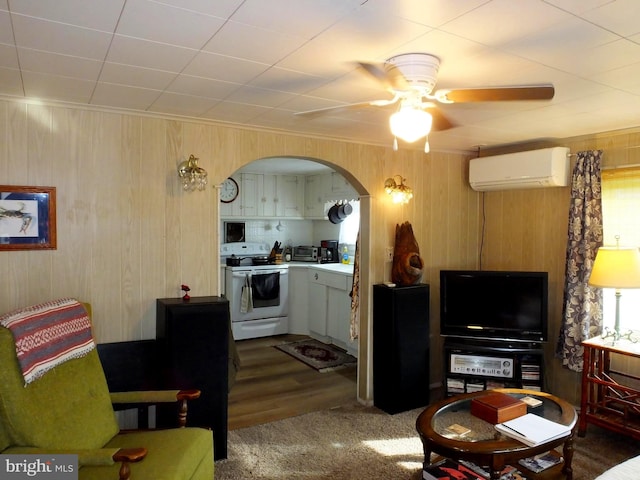 kitchen with ceiling fan, dark wood-type flooring, a wall unit AC, wood walls, and electric stove