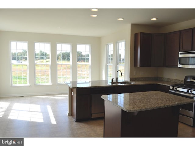 kitchen with appliances with stainless steel finishes, a center island, light stone counters, and sink