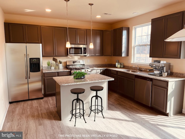 kitchen with sink, a center island, decorative light fixtures, appliances with stainless steel finishes, and light wood-type flooring