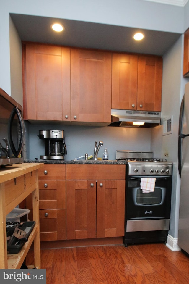 kitchen with stainless steel appliances, dark hardwood / wood-style floors, dark stone counters, and sink