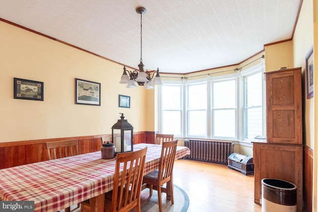 dining space featuring radiator, a textured ceiling, crown molding, an inviting chandelier, and hardwood / wood-style floors