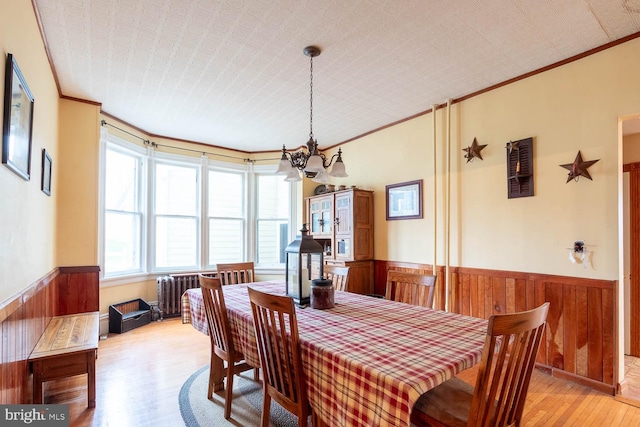 dining area featuring radiator, crown molding, light hardwood / wood-style flooring, and a notable chandelier