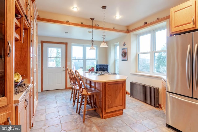 kitchen with radiator heating unit, hanging light fixtures, stainless steel fridge, a breakfast bar, and a kitchen island