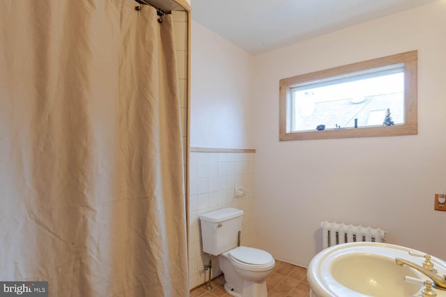 bathroom featuring radiator, sink, tile patterned flooring, toilet, and tile walls