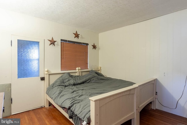 bedroom featuring hardwood / wood-style floors, a textured ceiling, and wood walls