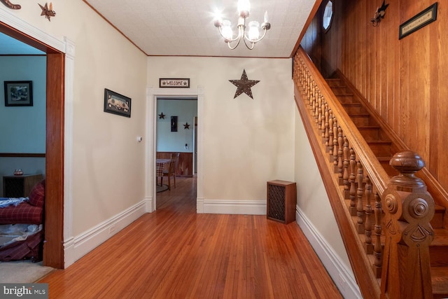 hall with ornamental molding, light wood-type flooring, an inviting chandelier, and wooden walls