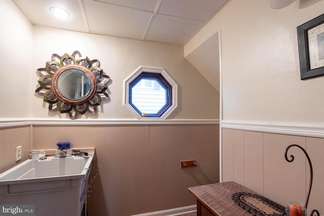 bathroom featuring wooden walls, a drop ceiling, and vaulted ceiling