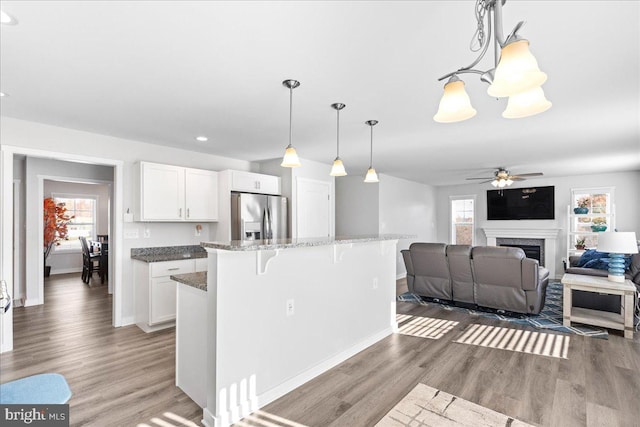 kitchen with dark hardwood / wood-style floors, decorative light fixtures, a breakfast bar area, white cabinets, and stainless steel fridge