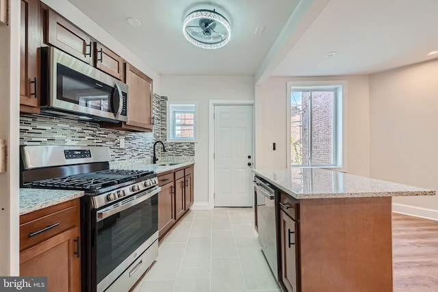 kitchen with sink, stainless steel appliances, a center island, tasteful backsplash, and light stone counters