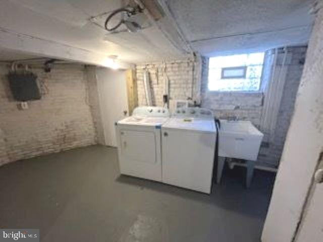 basement featuring brick wall, washer and dryer, and sink