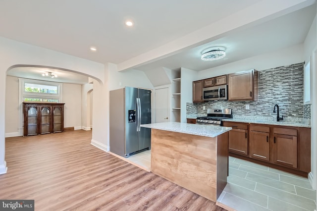 kitchen featuring a kitchen island, backsplash, stainless steel appliances, light stone countertops, and light hardwood / wood-style flooring