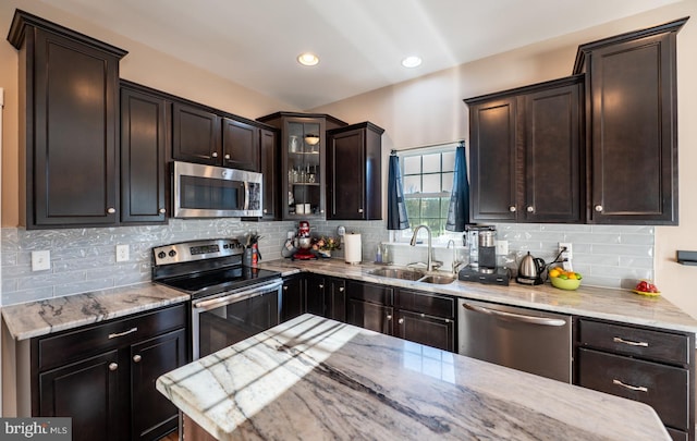 kitchen with appliances with stainless steel finishes, backsplash, light stone counters, dark brown cabinetry, and sink