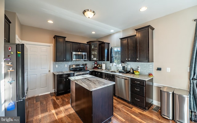 kitchen featuring light stone countertops, sink, dark wood-type flooring, stainless steel appliances, and a kitchen island