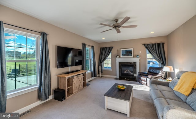 carpeted living room with ceiling fan, a fireplace, and a healthy amount of sunlight