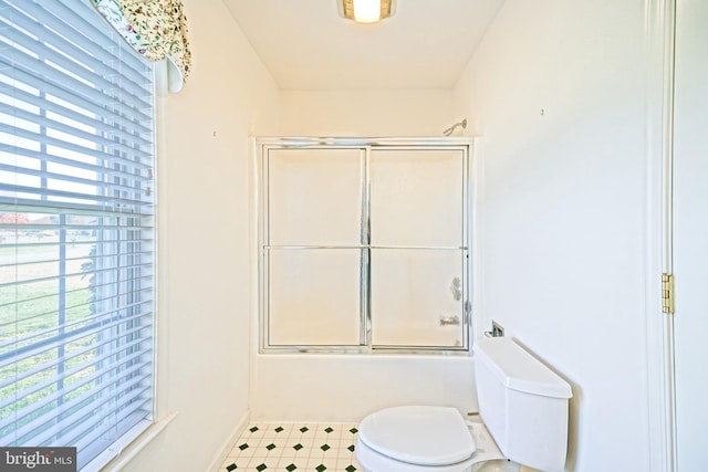 bathroom featuring a healthy amount of sunlight, toilet, and bath / shower combo with glass door