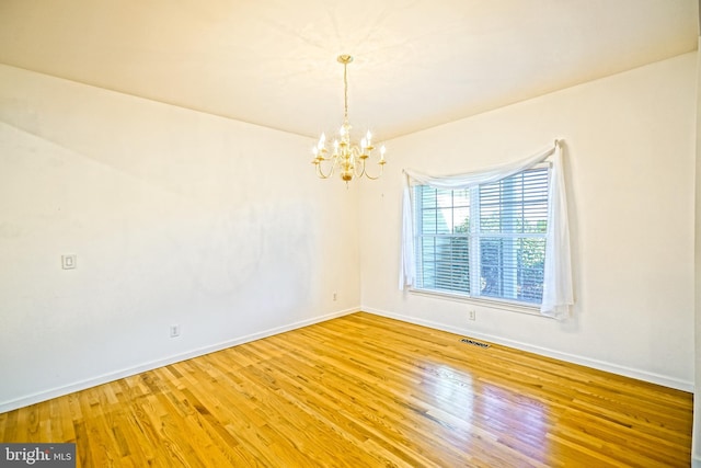 empty room with hardwood / wood-style floors and an inviting chandelier