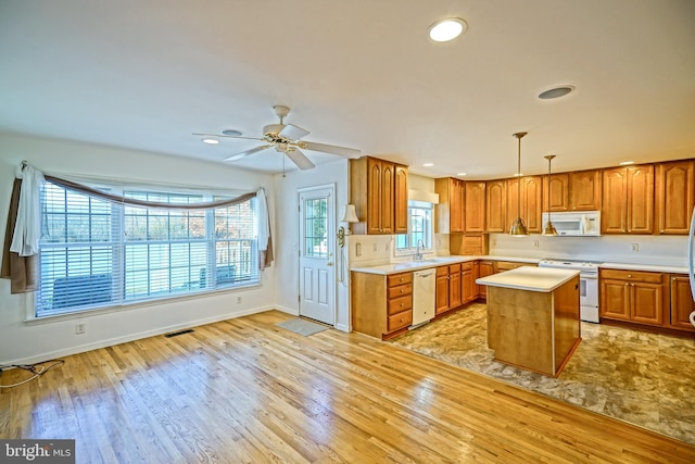 kitchen featuring white appliances, sink, a kitchen island, decorative light fixtures, and light hardwood / wood-style floors