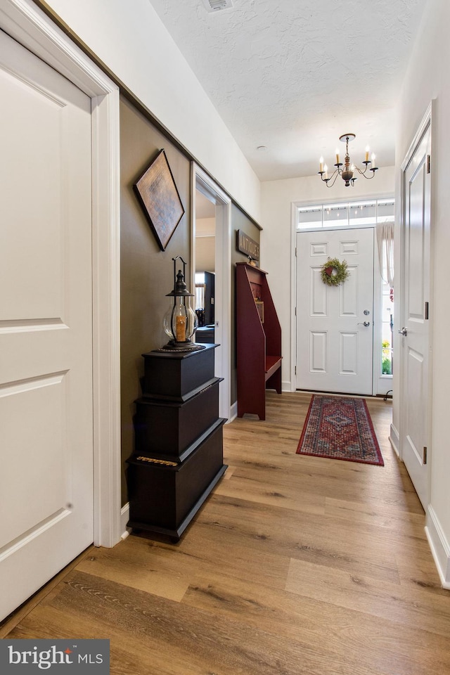 foyer entrance featuring an inviting chandelier, hardwood / wood-style floors, and a textured ceiling