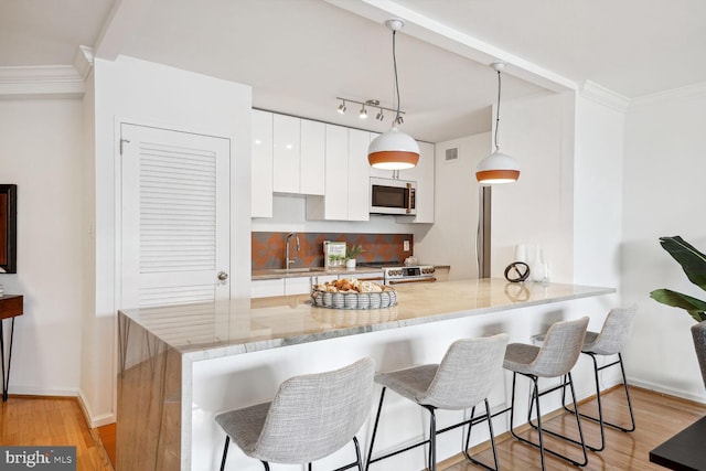 kitchen featuring kitchen peninsula, white cabinetry, decorative light fixtures, and appliances with stainless steel finishes